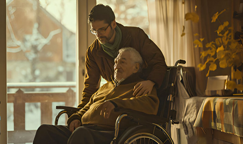 A kind caregiver standing behind an elderly man in a wheelchair, providing Respite and Live-In Care.